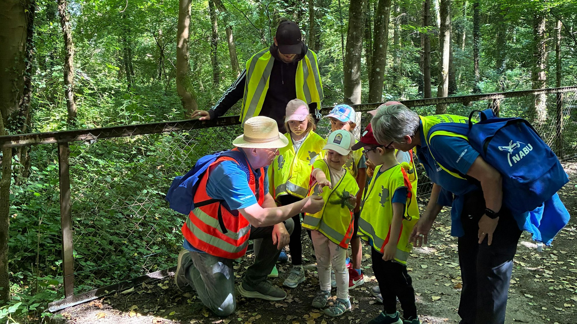 Zwei Senioren stehen mit Kindergartenkindern im Wald.