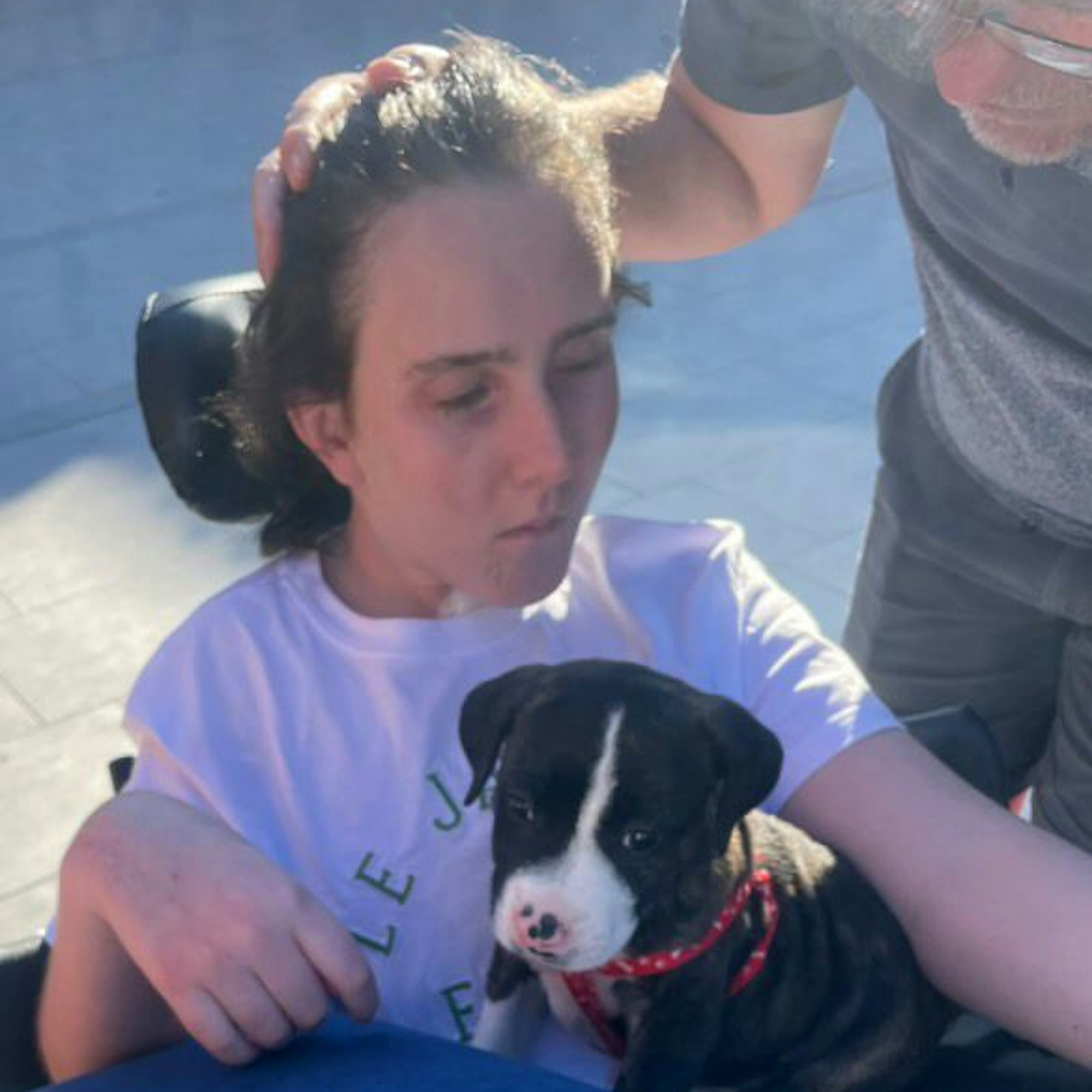 Jessie Munton sitzt in einem Rollstuhl, auf ihrem Schoß sitzt ein kleiner Hund.