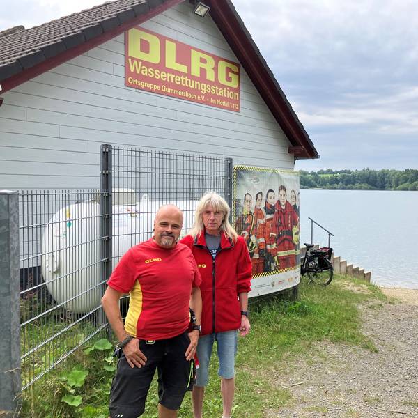 Ein Mann und eine Frau stehen vor einer Wachstation der DLRG an einem Badesee.