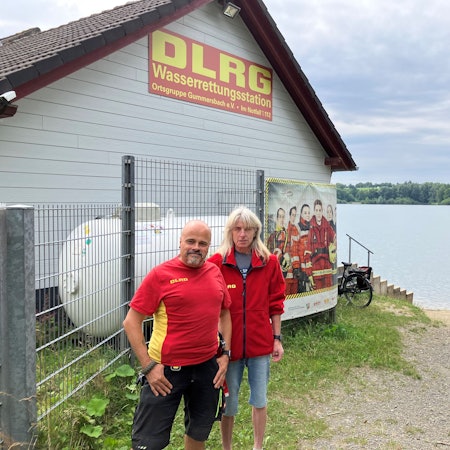 Ein Mann und eine Frau stehen vor einer Wachstation der DLRG an einem Badesee.
