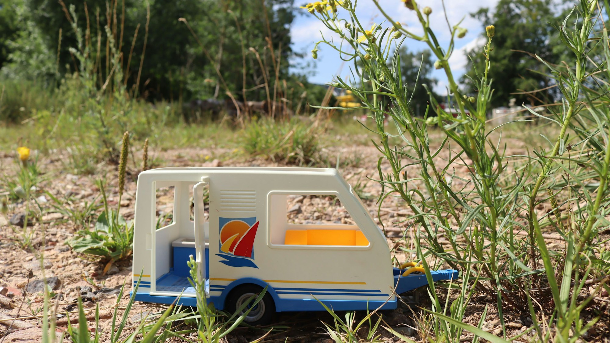 Ein kleiner Spielzeug-Wohnwagen steht auf einem leeren Feld zwischen ein paar Pflanzen in Bad Münstereifel.