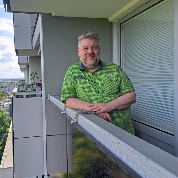 Ein Mann lehnt an der Brüstung seines Balkons, an dem ein Solarmodul angebracht ist.
