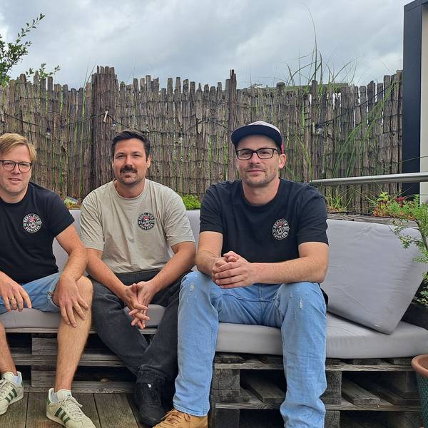 Vier Männer in den 30ern sitzen nebeneinander auf einem Outdoor-Sofa.