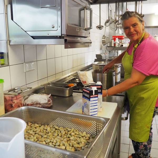 Monika Bärhausen trägt ein pinkes Shirt und eine grüne Schürzte. Sie arbeitet am Herd in der Küche der Gaststätte Watteler im Freilichtmuseum Kommern.