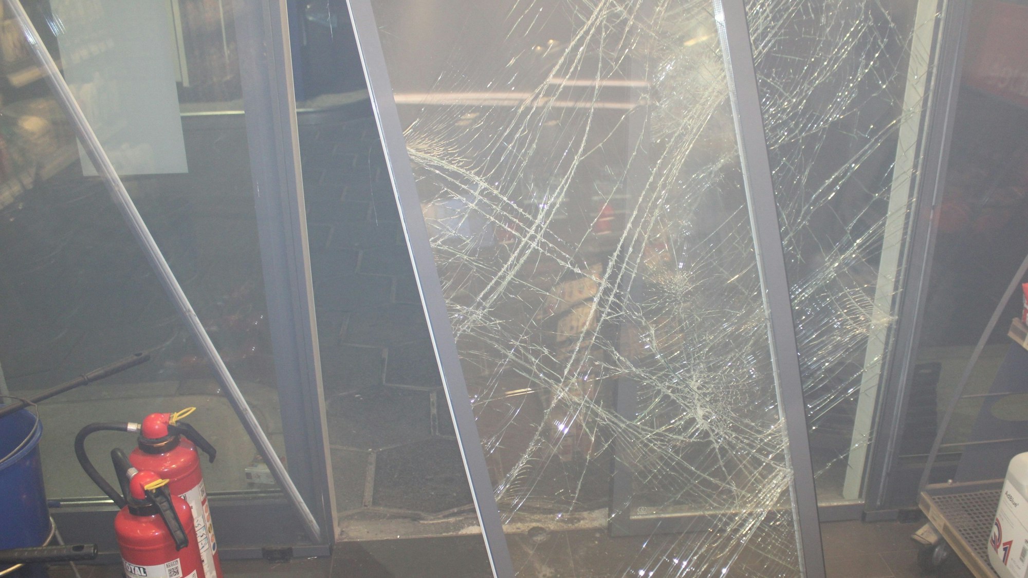 Das Bild zeigt eine zertrümmerte Eingangstür aus Glas.