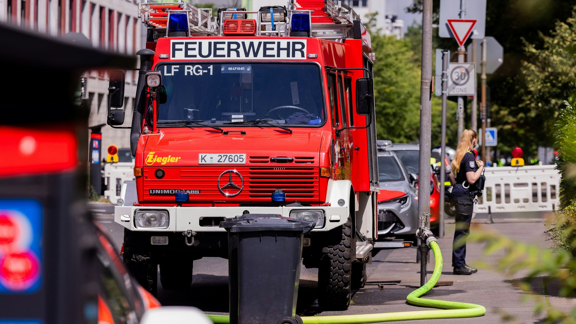 17.07.2025, Nordrhein-Westfalen, Köln: Die Feuerwehr hält sich bereit, um Container mit Wasser zu befüllen, die zum Schutz an der Fundestelle einer Weltkriegsbombe am Lindenhof unweit der Universitätsklinik aufgestellt worden sind. Ein Blindgänger aus dem Zweiten Weltkrieg soll entschärft werden. Im 400-Meter-Radius müssen rund 7.500 Anwohnende evakuiert werden, auch die Uniklinik ist betroffen. Foto: Rolf Vennenbernd/dpa +++ dpa-Bildfunk +++