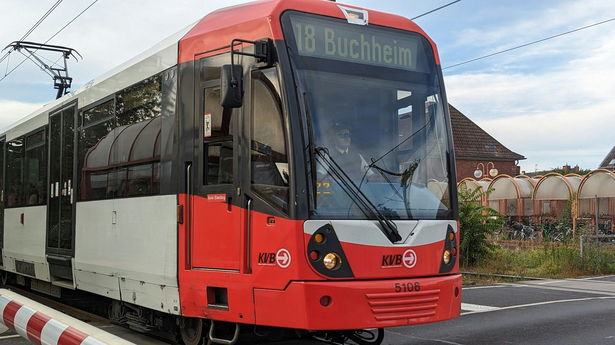 Eine Straßenbahn der Linie 18, Richtung Buchheim, fährt an einer niedergelassenen Schranke vorüber.