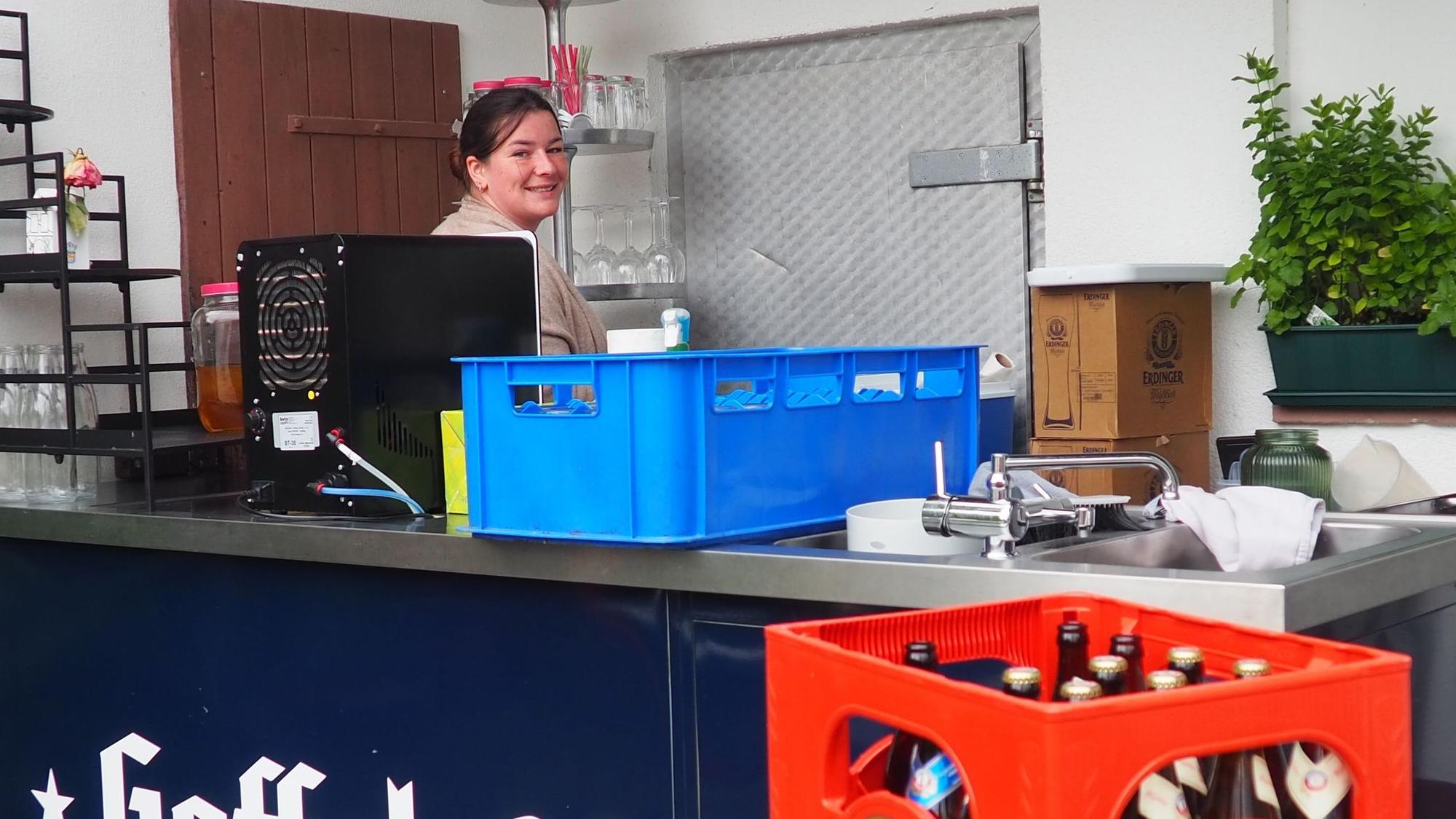 Joanna Bärhausen steht an einer Theke, auf der eine Zapfanlage steht. Vorne sind Bierkästen zu erkennen.