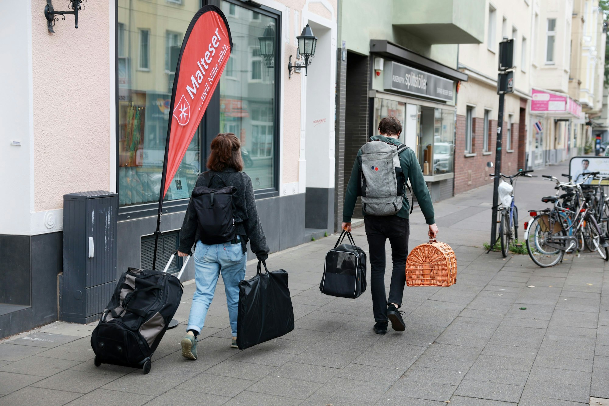 Menschen gehen mit Taschen über einen Bürgersteig.