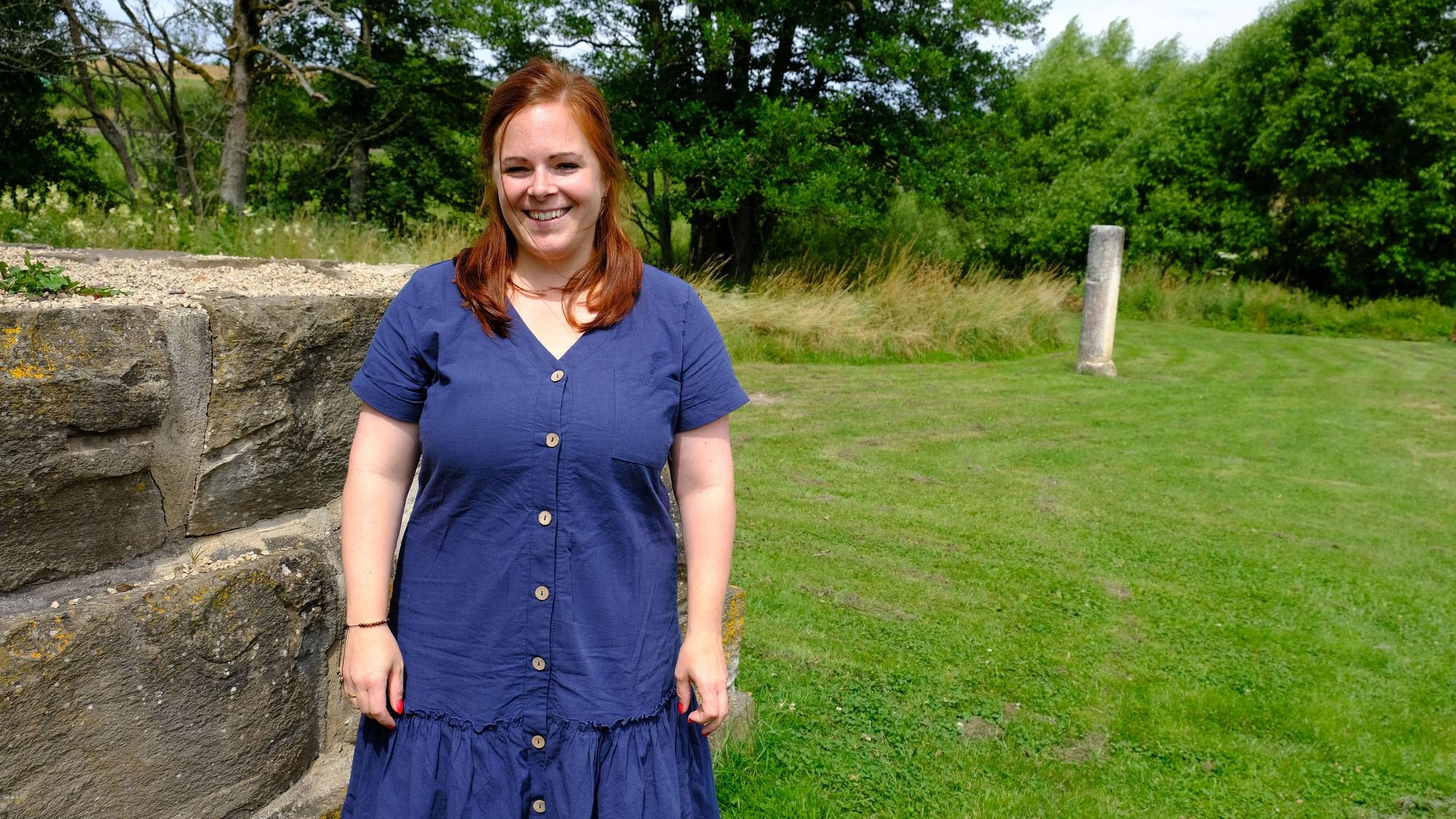 Die Archäologin Linda Lorbach am römischen Kleinkastell am Steinrütsch bei Nettersheim; sie trägt ein blaues Kleid.