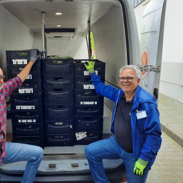Zwei Männer stehen an einem geöffneten Transporter, in dem Lebensmittelkisten stehen.