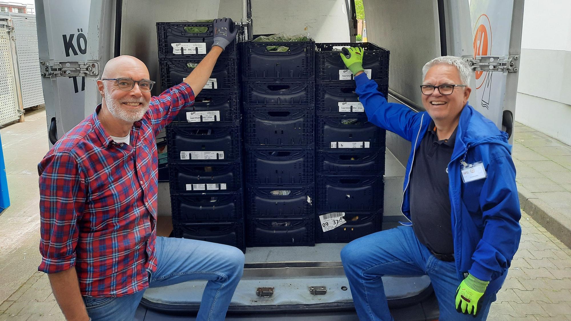 Zwei Männer stehen an einem geöffneten Transporter, in dem Lebensmittelkisten stehen.