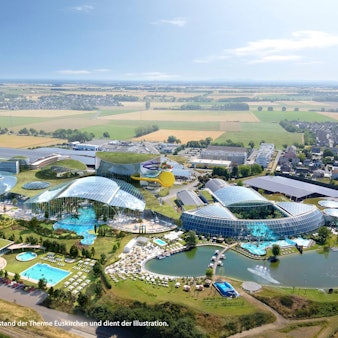 Das Bild zeigt die Anlage aus der Luft. Sie besteht aus mehreren verglasten Gebäuden, Grünflächen und Teichen.