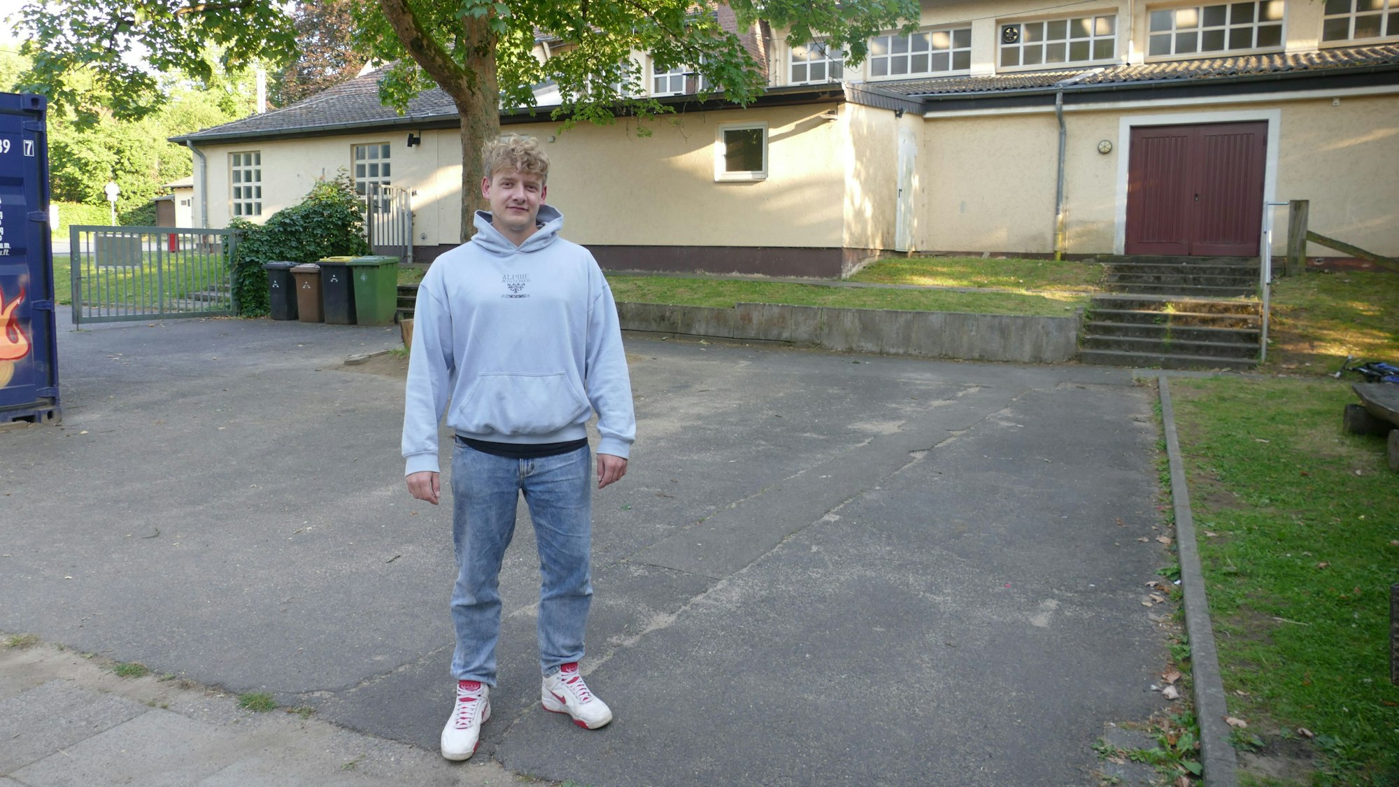 Ein Mann im Hoodie steht in einem asphaltierten Hof.