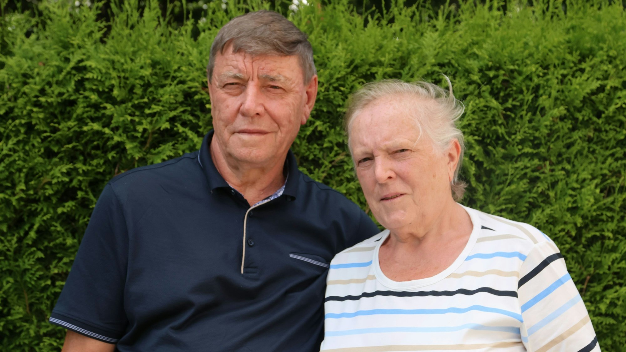 Ein älteres Paar vor einer Hecke.