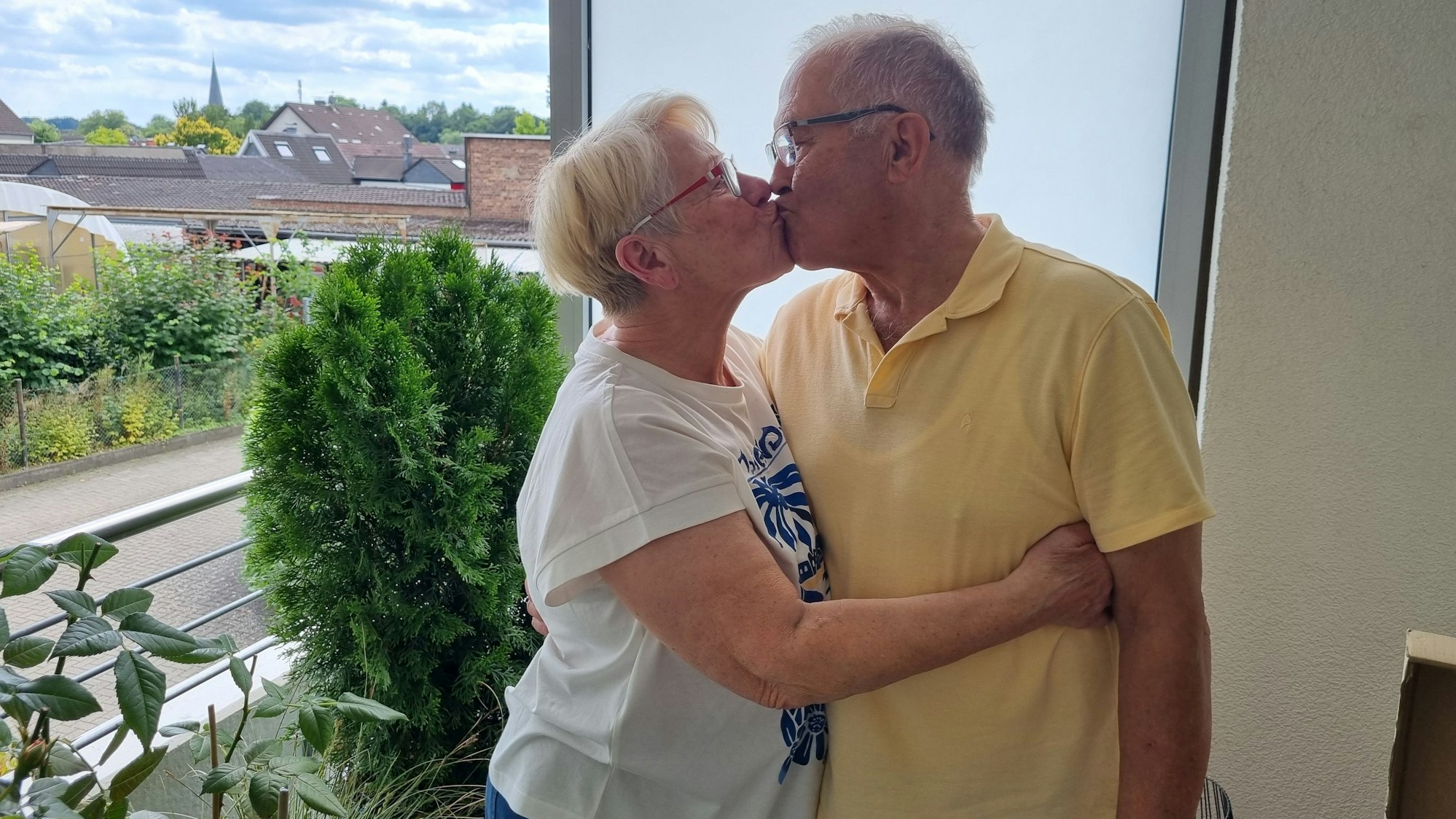 Zwei Menschen stehen auf einem Balkon und geben sich einen Kuss.