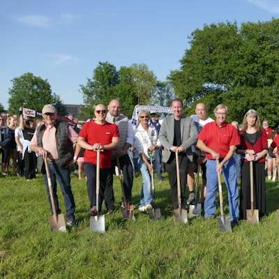 Männer und Frauen stehen mit Spaten auf einer Wiese.