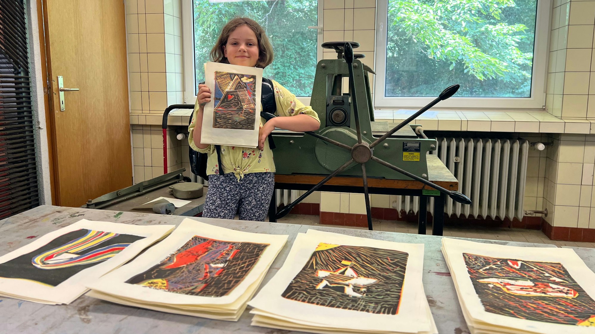 Ein Kind zeigt stolz künstlerische Arbeiten von sich.