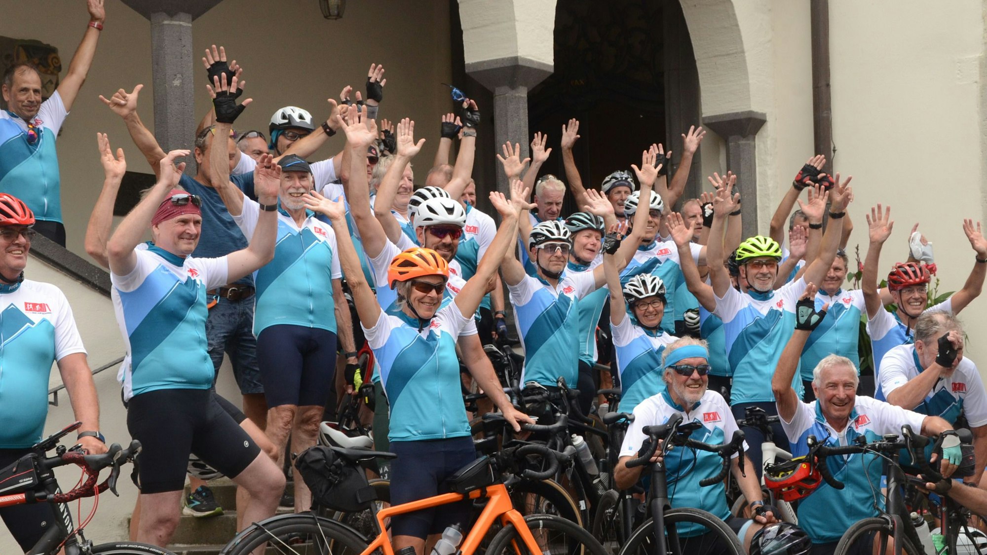 Männer und Frauen in Rennradtrikots werfen die Hände in die Luft.