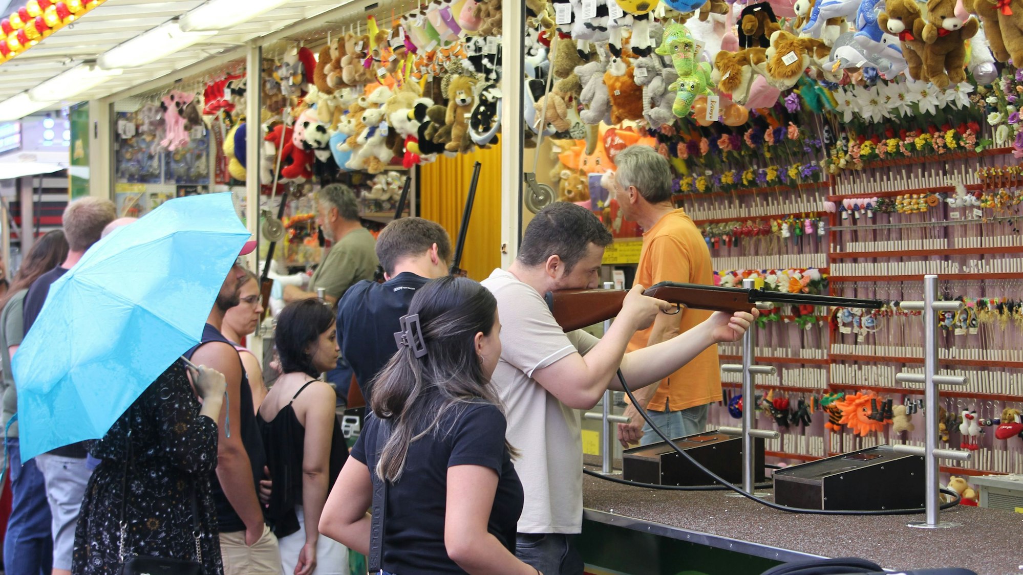 Auf dem Bild sind Kirmesbesucher vor eine Schießstand zu sehen.