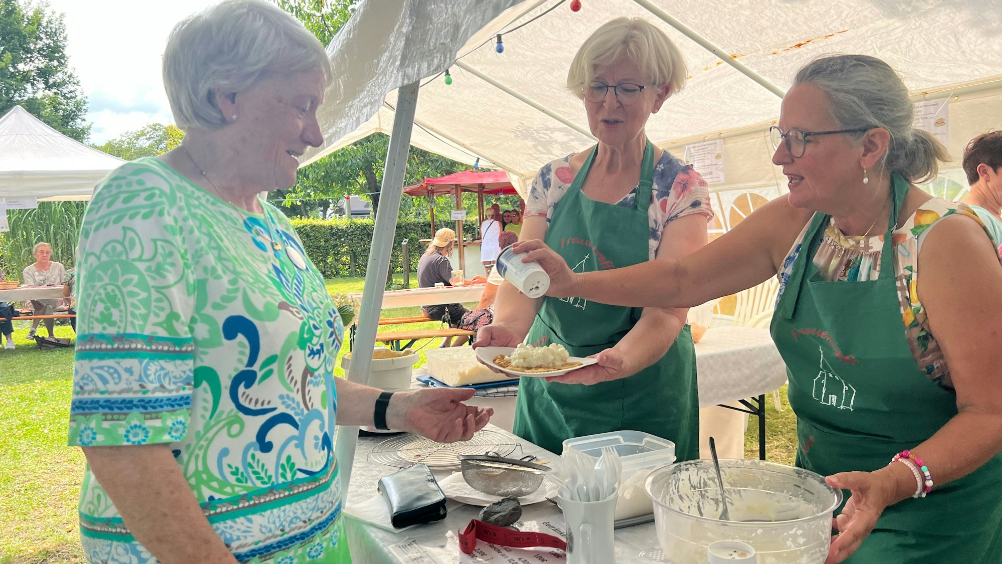 Zwei Frauen geben einer weiteren Frau einen Teller mit Waffel und Reisbrei.