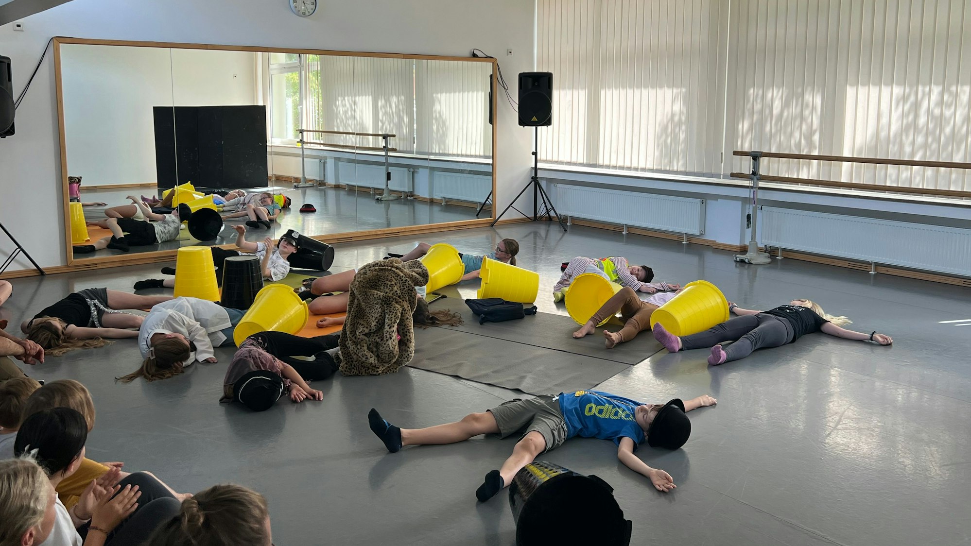 Kinder liegen während eines Theaterstücks vor einem großen Spiegel auf dem Boden.