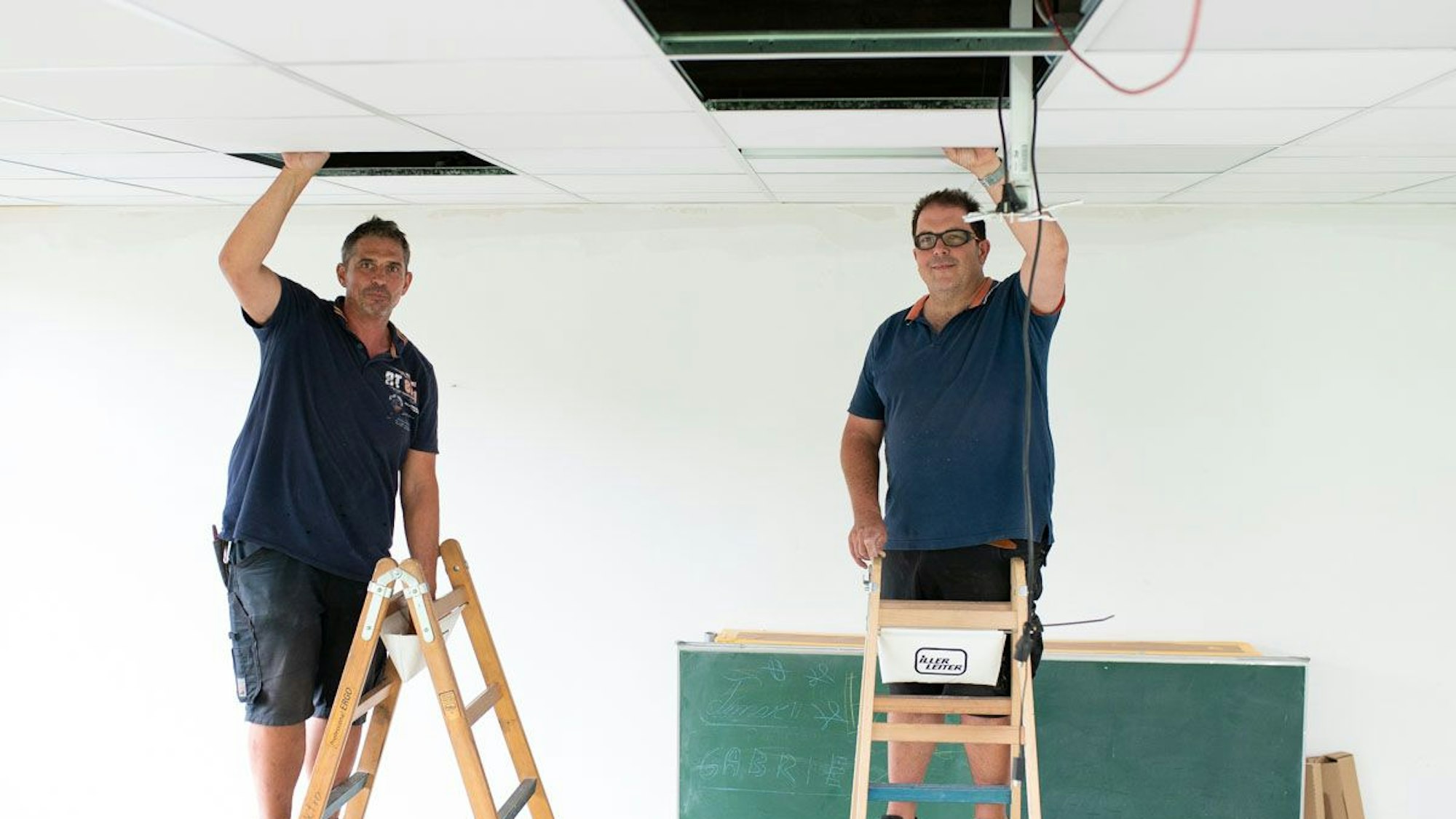 Auf dem Bild sind zwei Handwerker in einer Schule zu sehen.