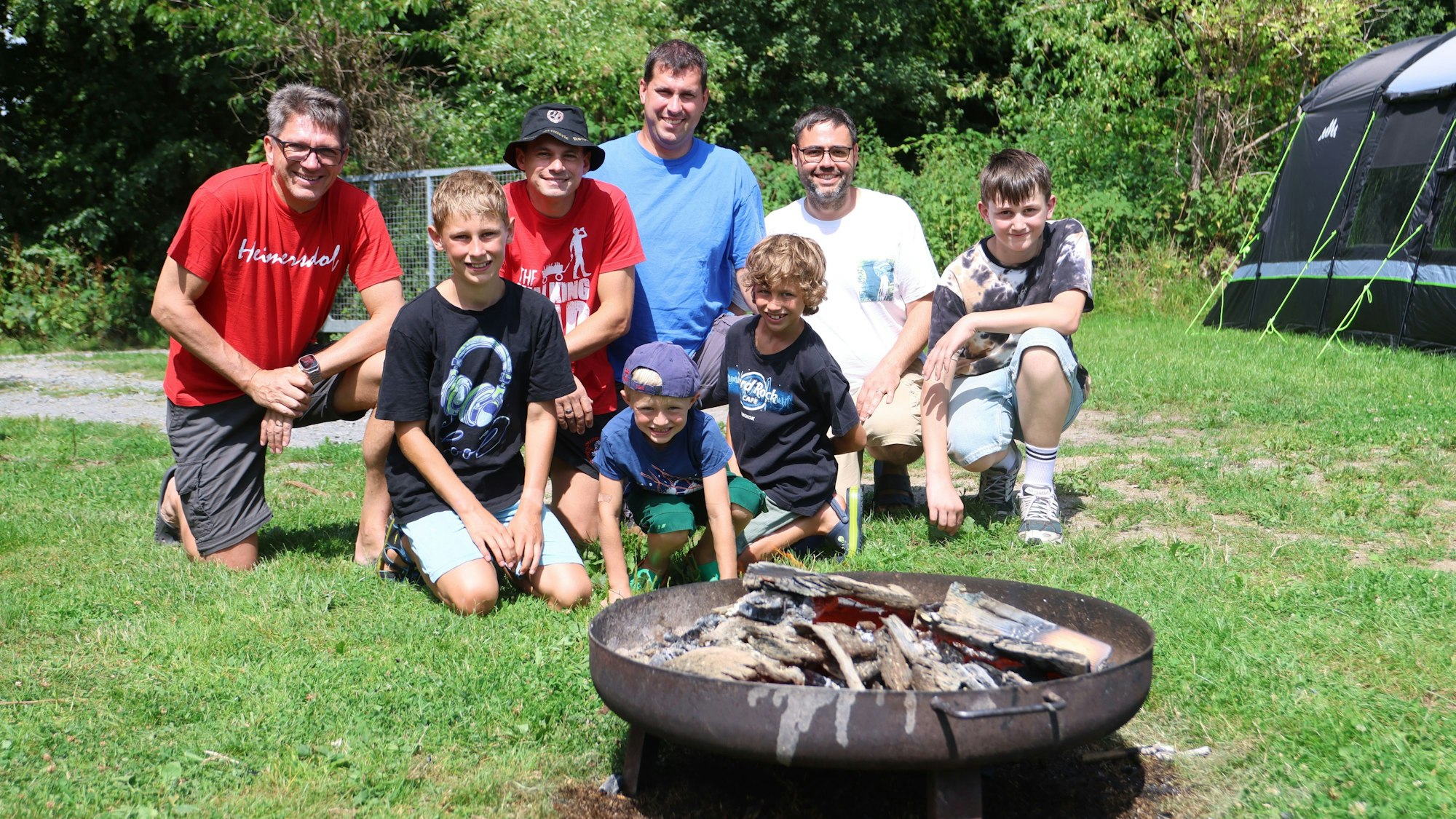 Männer und Jungen posieren vor einer Feuerschale.
