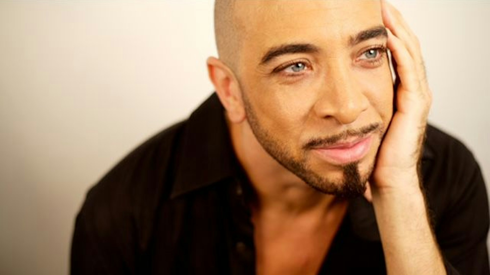 Das angeschnittenes Porträtfoto zeigt Dwight Rhoden lächelnd, den Kopf in der Handfläche haltend