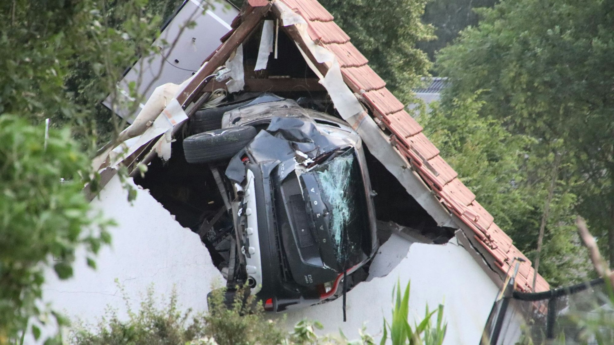 Ein Auto liegt nach einem kurzen Flug seitlich in der Mauer einer Scheune.