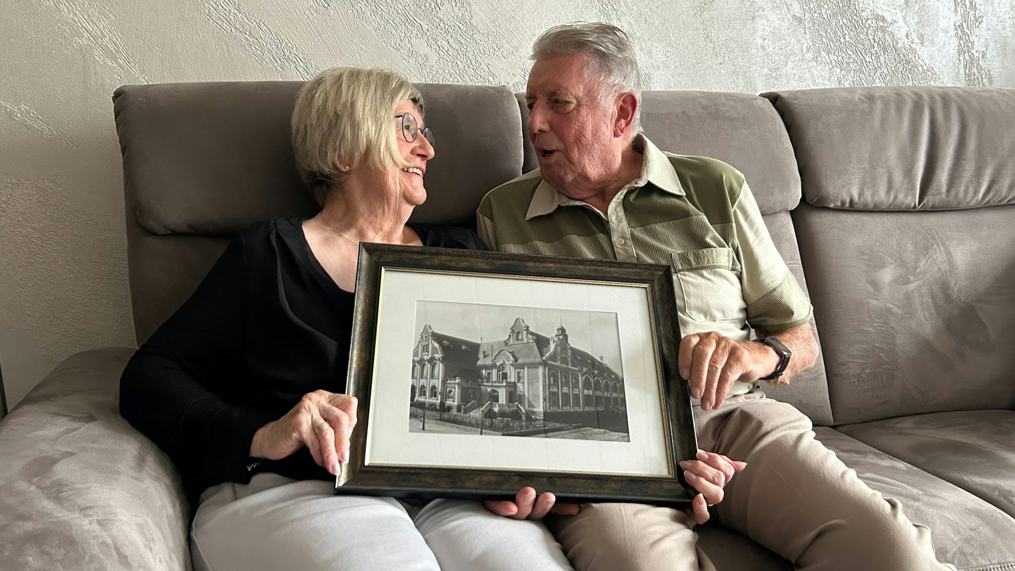 Ein älteres Ehepaar sitzt auf einem Sofa mit einem Foto in der Hand.