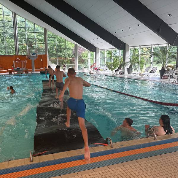 Kinder laufen in einem Hallenbad über eine Laufmatte auf dem Wasser.