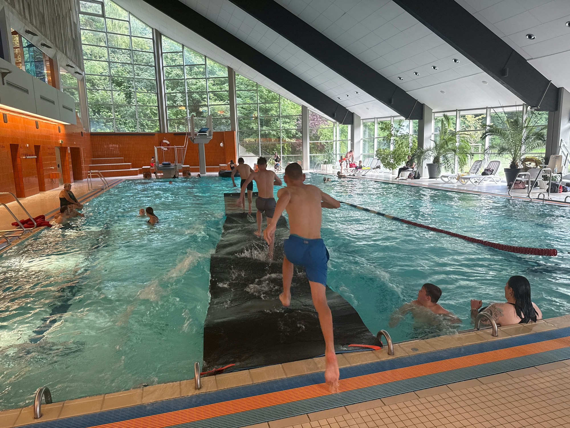 Kinder laufen in einem Hallenbad über eine Laufmatte auf dem Wasser.