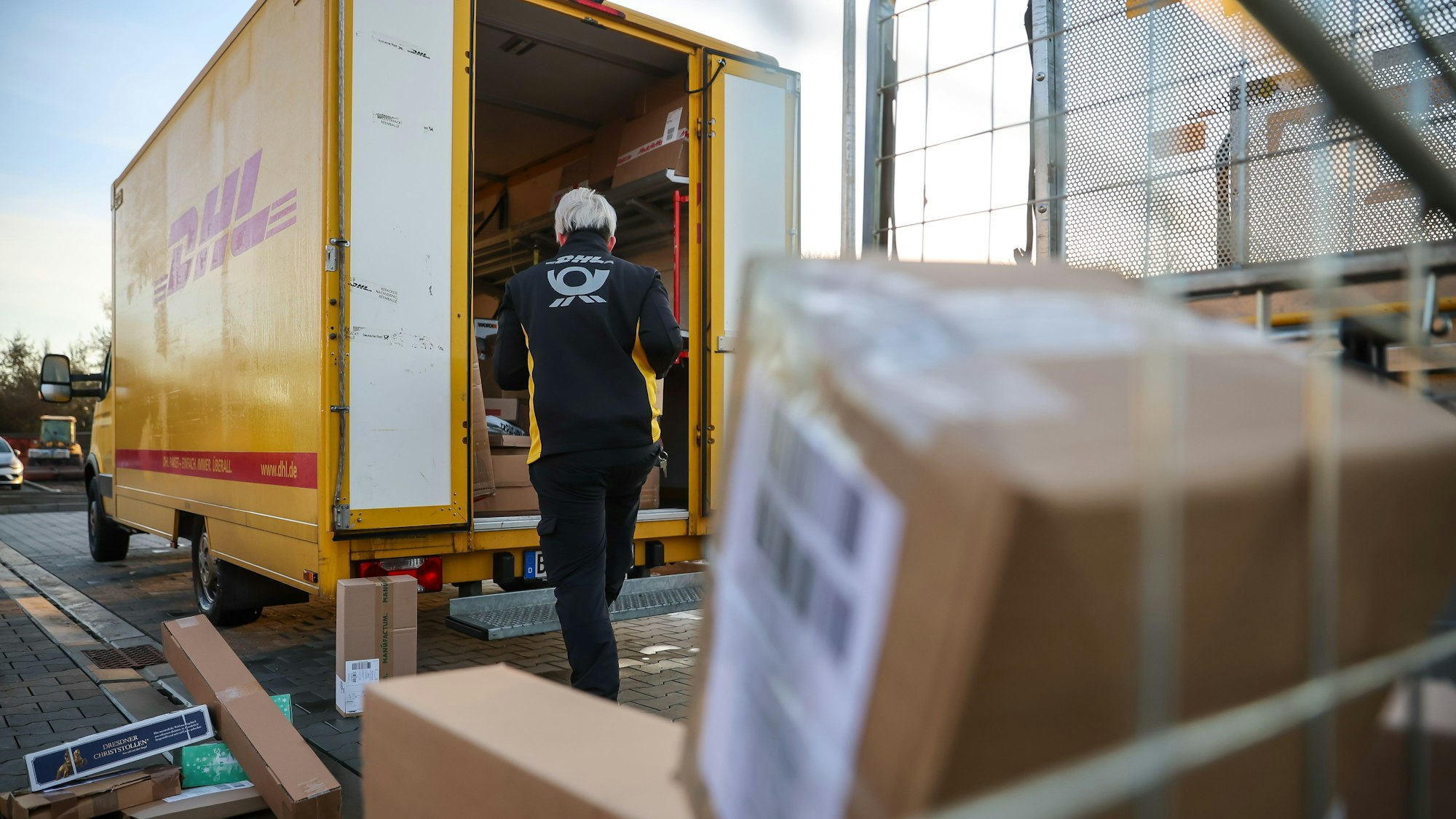 Eine Mitarbeiterin der Deutsche Post DHL belädt ihr Fahrzeug mit Päckchen und Paketen. (Archivbild)