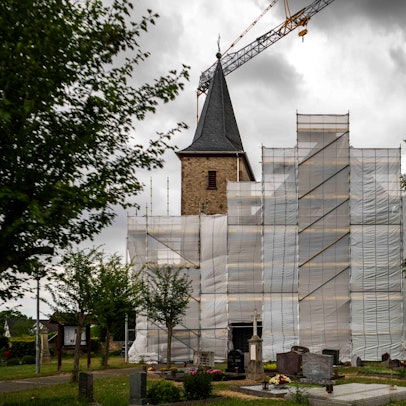 Die Kirche in Lövenich wird seit Jahren saniert. Das Haupthaus ist eingerüstet und mit Planen verhängt.