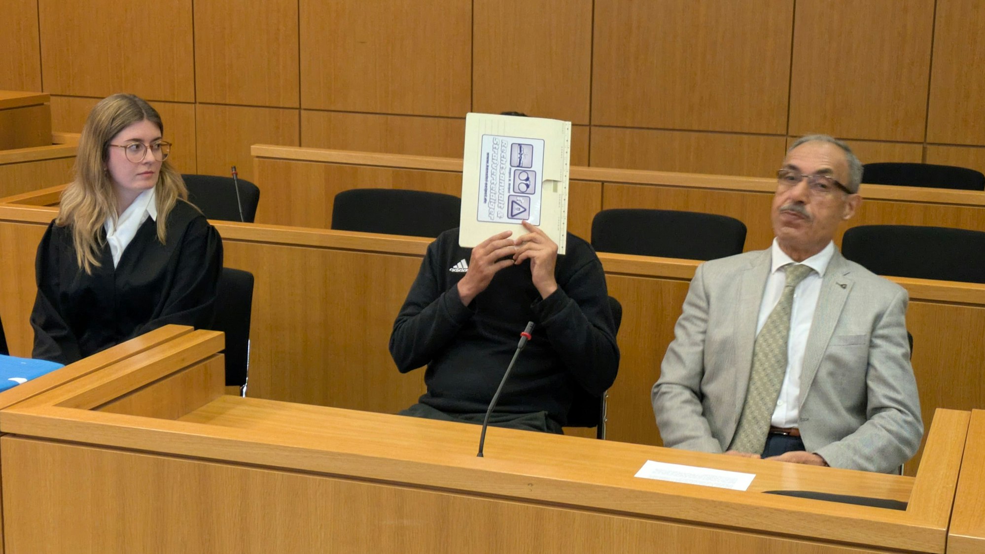 Der Angeklagte hält sich in einem Gerichtssaal in Aachen einen Aktendeckel vors Gesicht.