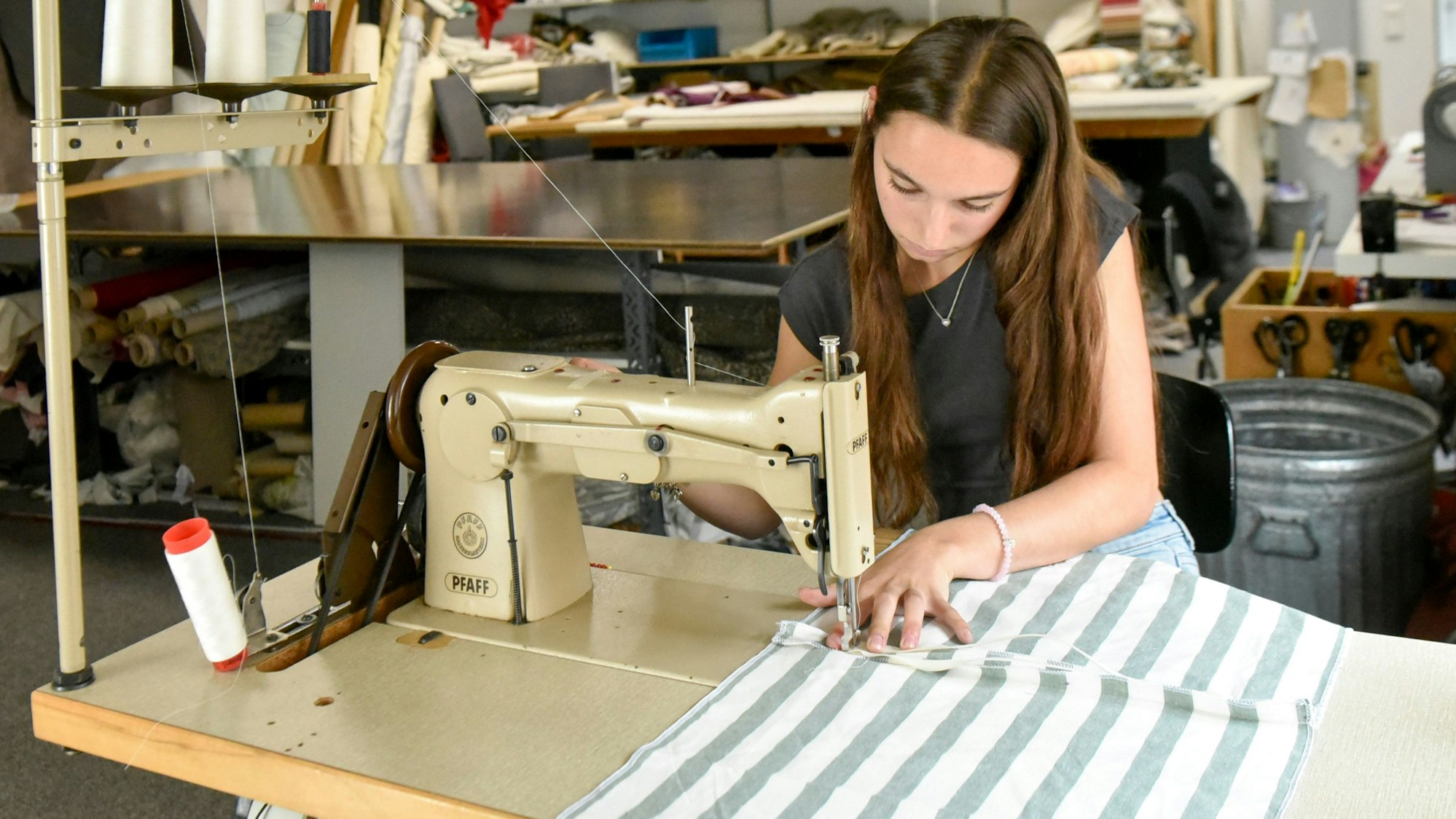 Zu sehen ist eine Frau an einer Nähmaschine.