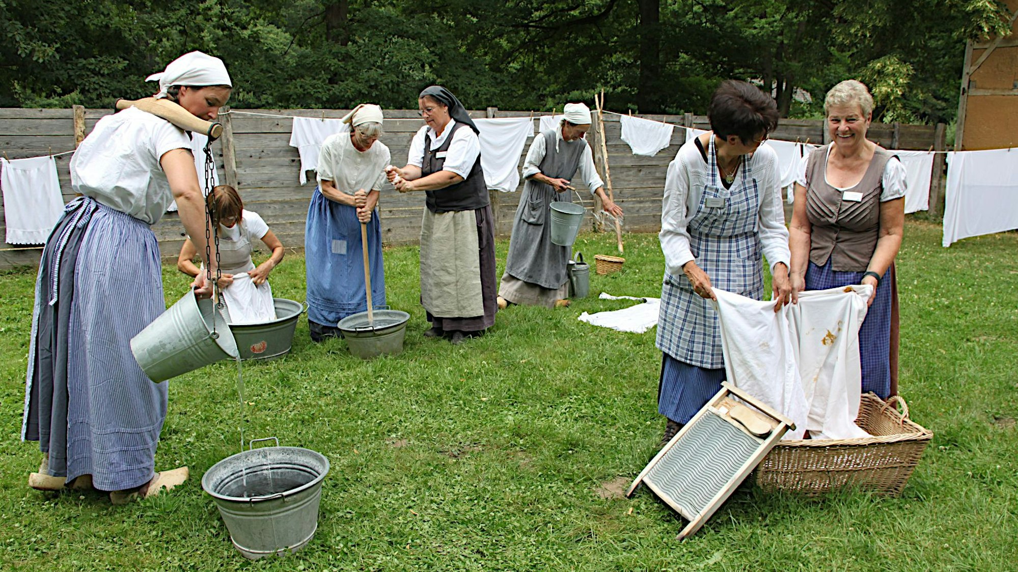 Frauen in historischer Kostümierung stehen an Waschbrettern und waschen Leinenzeug.