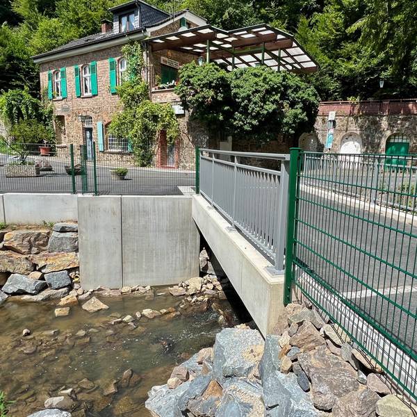 Eine neue Brücke über einen Bach mit einem alten Haus im Hintergrund
