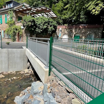 Eine neue Brücke über einen Bach mit einem alten Haus im Hintergrund