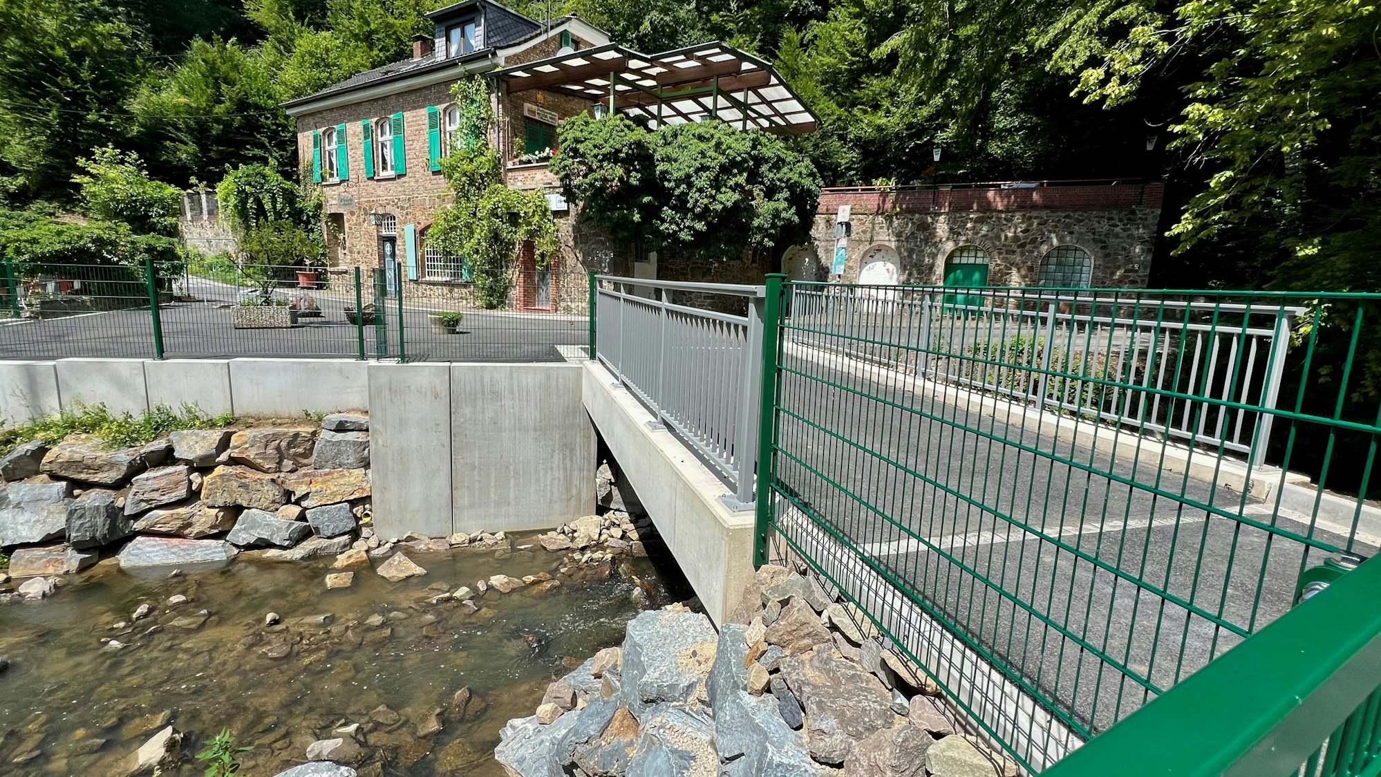 Eine neue Brücke über einen Bach mit einem alten Haus im Hintergrund