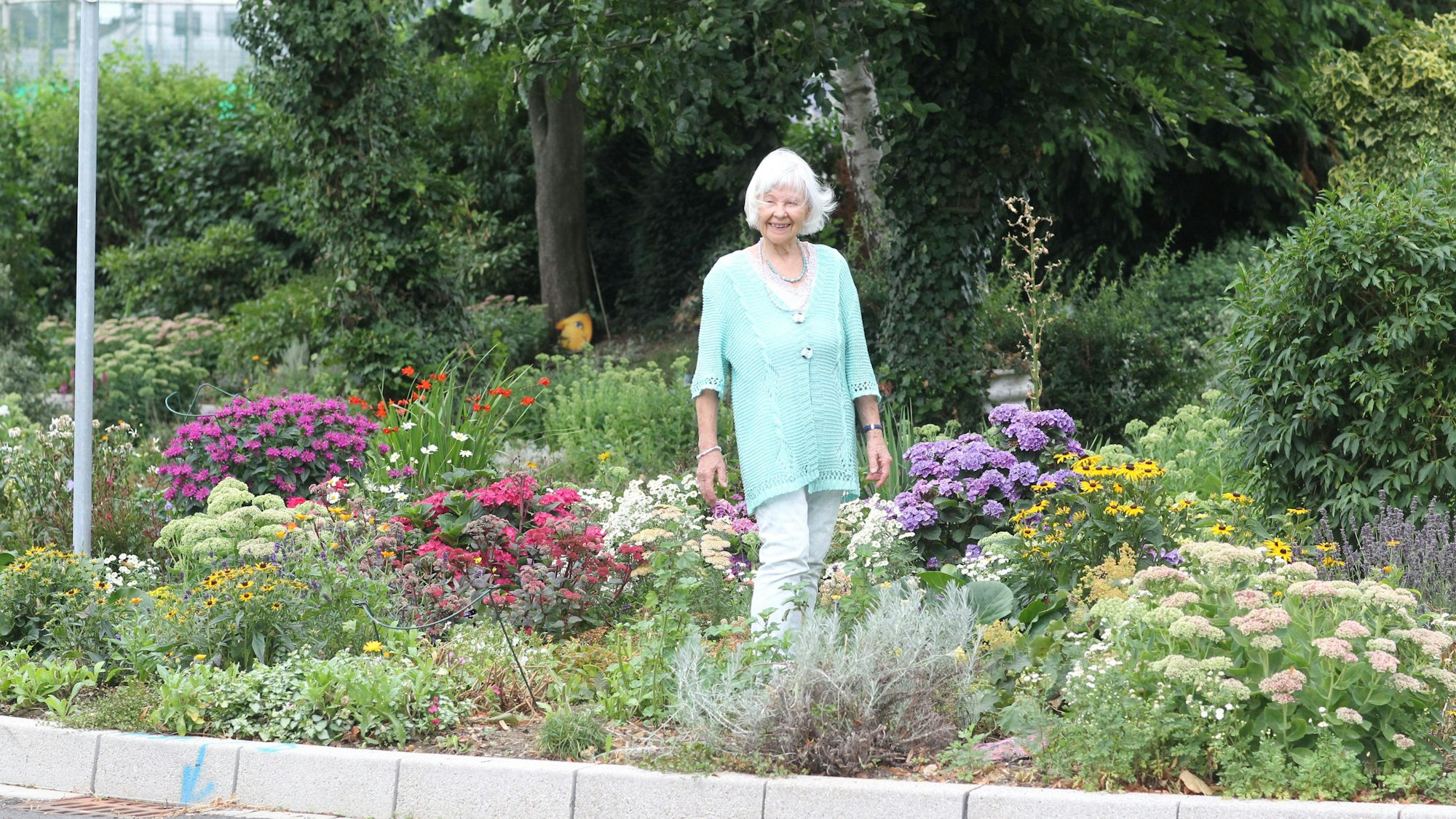 Gisela Pinunsko (85) steht in Winterscheid in dem Beet am Tennisplatz gegenüber der Kapelle, wo alles vor 20 Jahren begann.