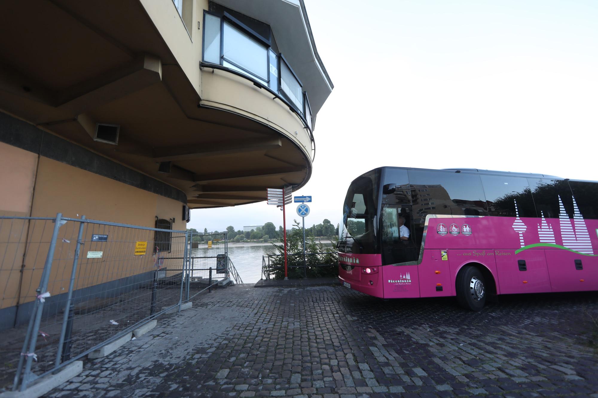 09.07.2025, Köln: Ein Reisebus steht vor einem Gebäude. Im Hintergrund befindet sich der Rhein.