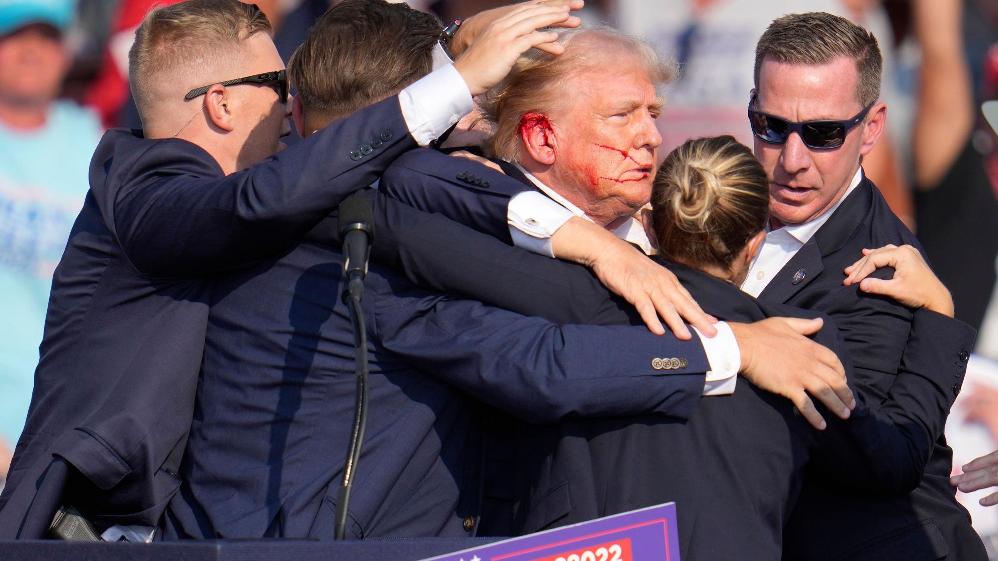 ARCHIV - 14.07.2024, USA, Butler: Der republikanische Präsidentschaftsbewerber und frühere US-Präsident Donald Trump wird von Agenten des US-Geheimdienstes Secret Service umringt, als ihm bei einer Wahlkampfveranstaltung von der Bühne geholfen wird. (zu dpa: «Schlussbericht zu Attentat auf Trump: «Gravierende Mängel»») Foto: Gene J. Puskar/AP/dpa +++ dpa-Bildfunk +++