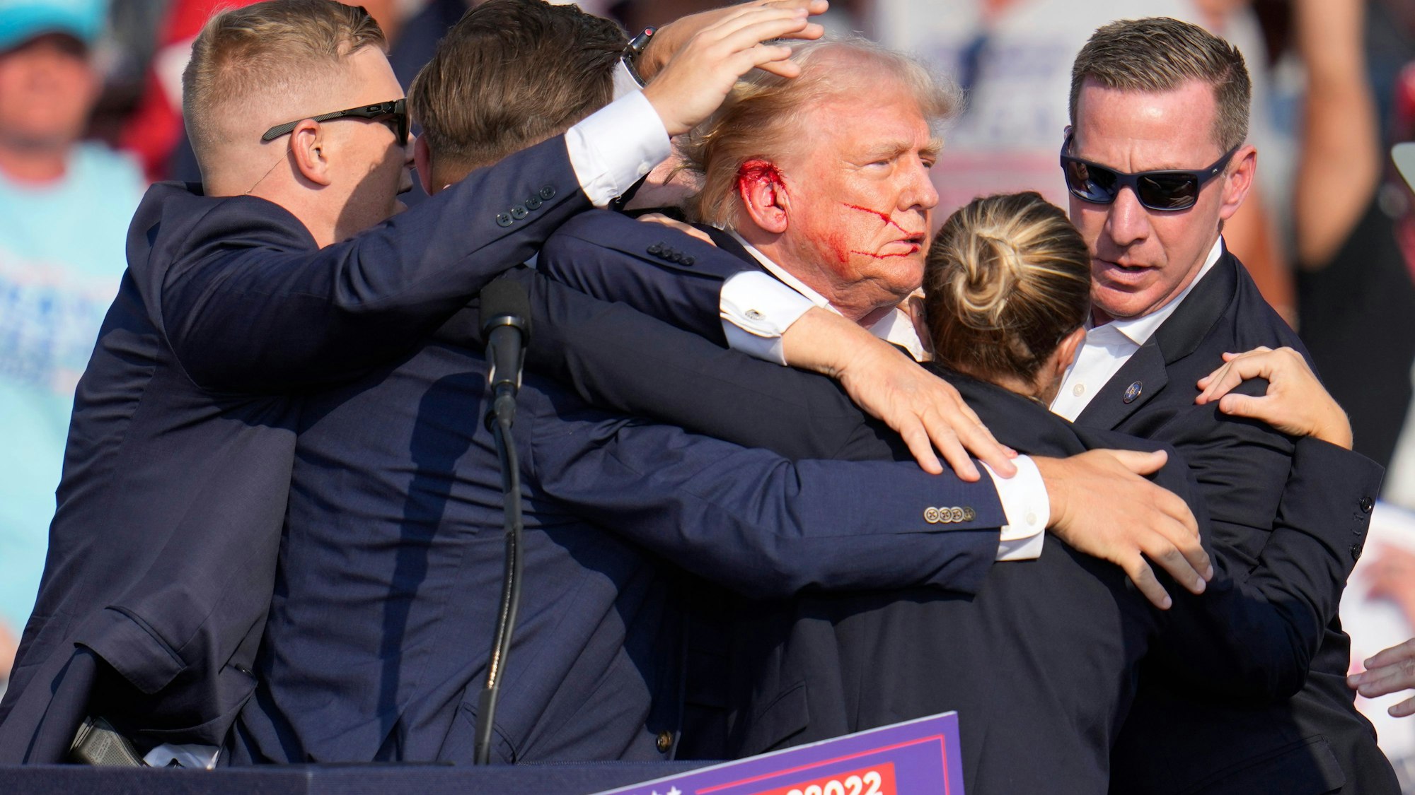 ARCHIV - 14.07.2024, USA, Butler: Der republikanische Präsidentschaftsbewerber und frühere US-Präsident Donald Trump wird von Agenten des US-Geheimdienstes Secret Service umringt, als ihm bei einer Wahlkampfveranstaltung von der Bühne geholfen wird. (zu dpa: «Schlussbericht zu Attentat auf Trump: «Gravierende Mängel»») Foto: Gene J. Puskar/AP/dpa +++ dpa-Bildfunk +++