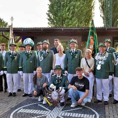 Eine Gruppe Männer steht in grün-weißer Schützen-Uniform und mit ein paar Frauen in ziviler Kleidung auf einem Platz.