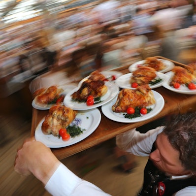 Ein Kellner trägt auf dem Oktoberfest Hendl (Hähnchen) auf einem Tablett durch ein Bierzelt.