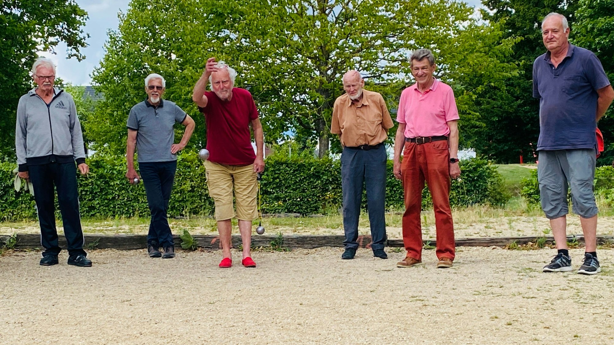 Sechs ältere Herren stehen an einer Boulebahn. Ein Spieler wirft gerade seine Kugel.