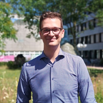 Thörner trägt eine Brille und ein blaues Hemd. Er steht vor dem Rathaus Bergheim.