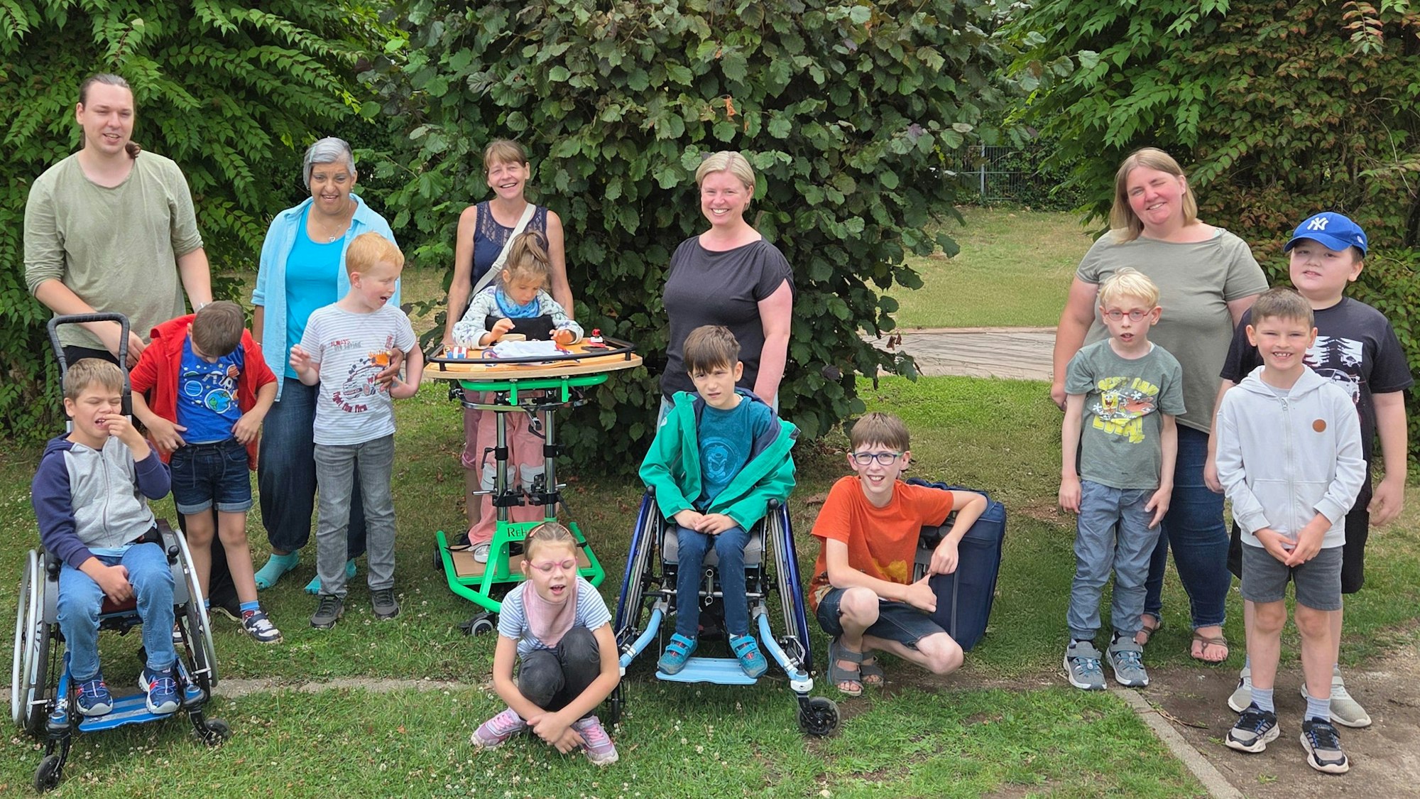 Kinder mit Behinderung und erwachsene Betreuer stehen und sitzen in einem Park.